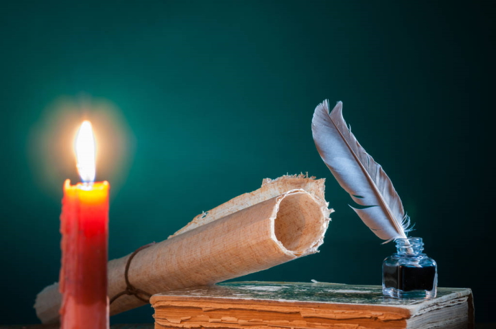 Quill pen and a rolled papyrus sheet on an old book by candle light